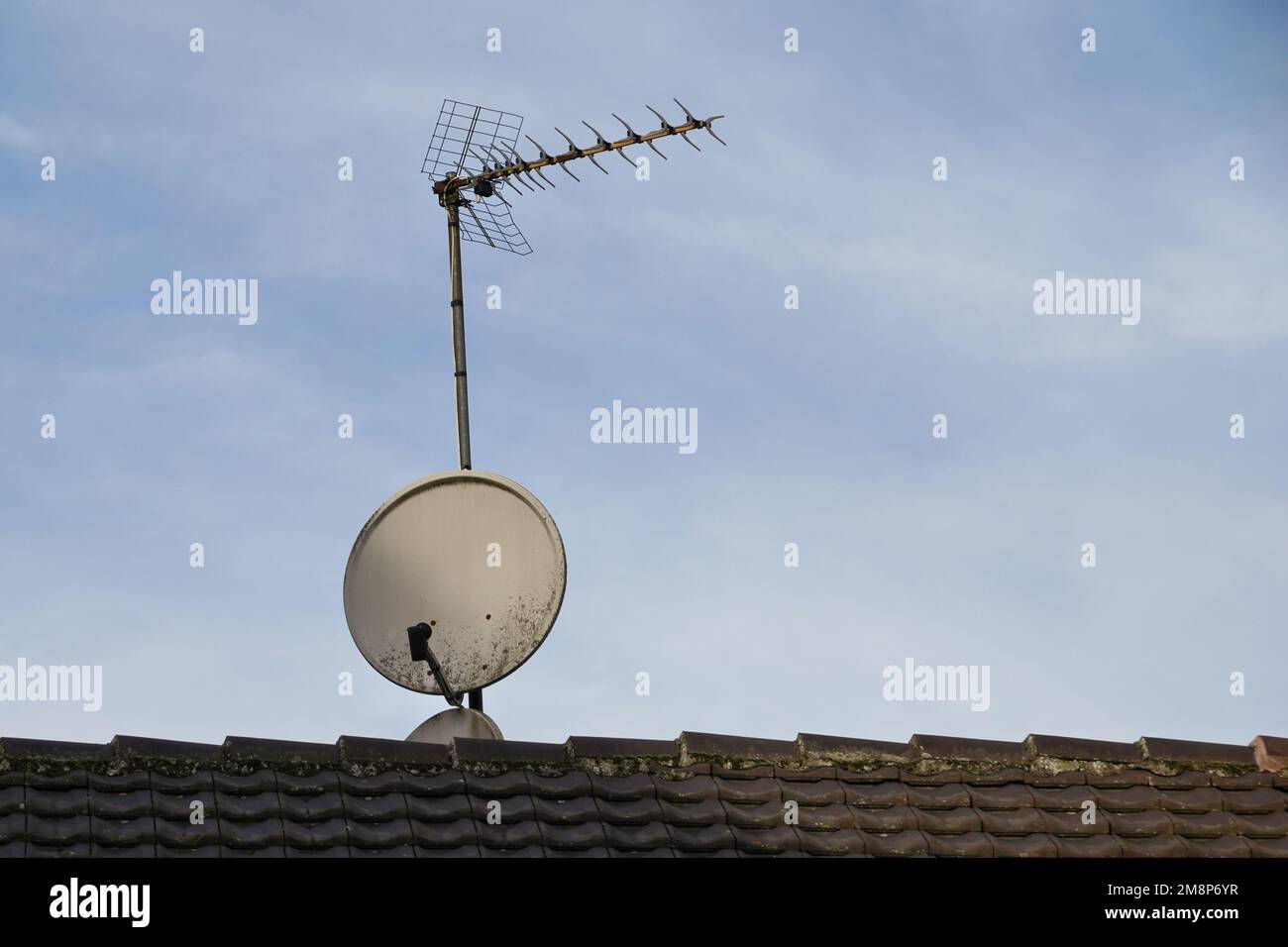 Analogue antenna and a satellite one are placed on a rooftop of a tiled roof. Stock Photo