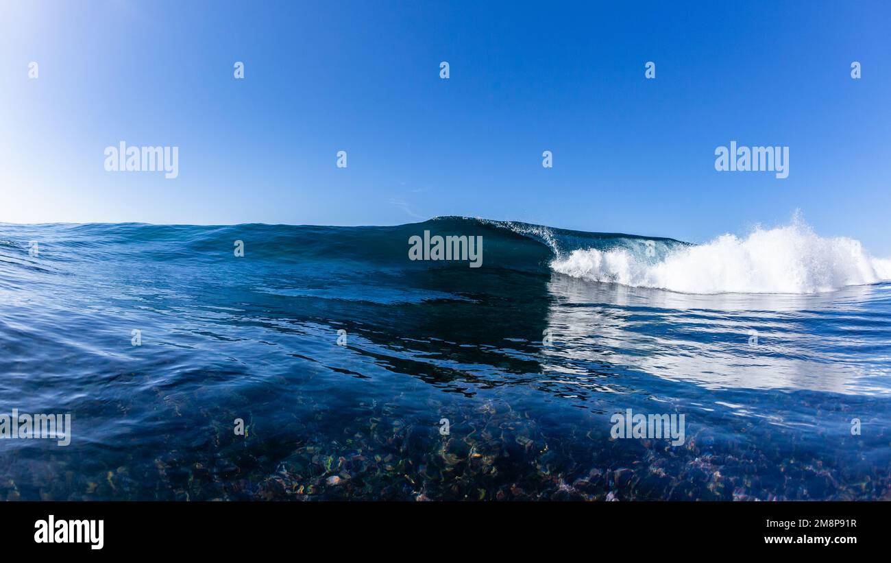 Ocean wave swimming close-up encounter hollow crashing blue water wave crashing on shallow rock coral reefs. Stock Photo
