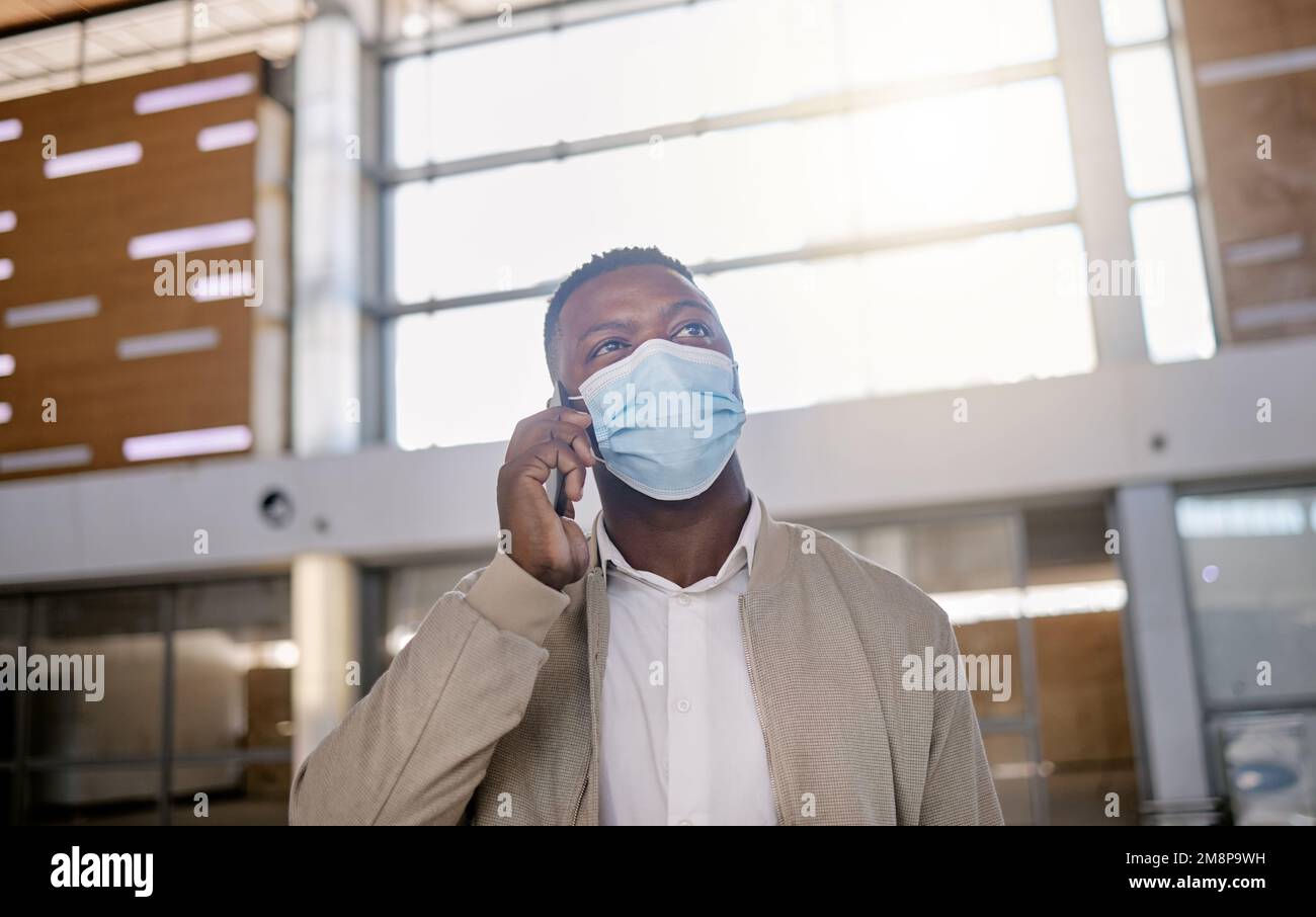 African american male on a phone call with his mobile device inside a station during the day while wearing a mask. Young black male talking on a phone Stock Photo