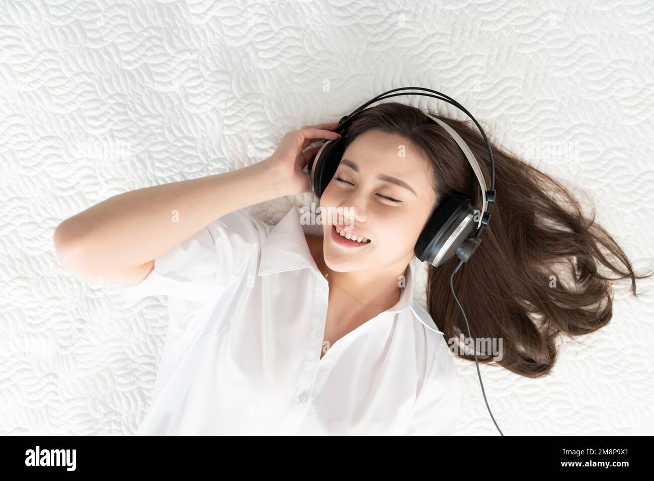 A young woman lying in bed listening to music Stock Photo - Alamy