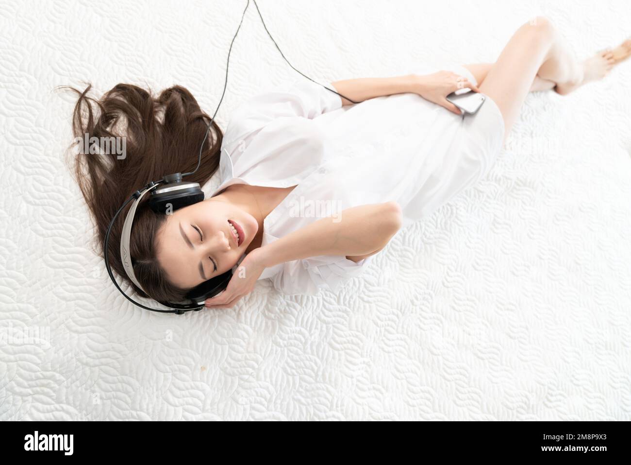 A young woman lying in bed listening to music Stock Photo - Alamy