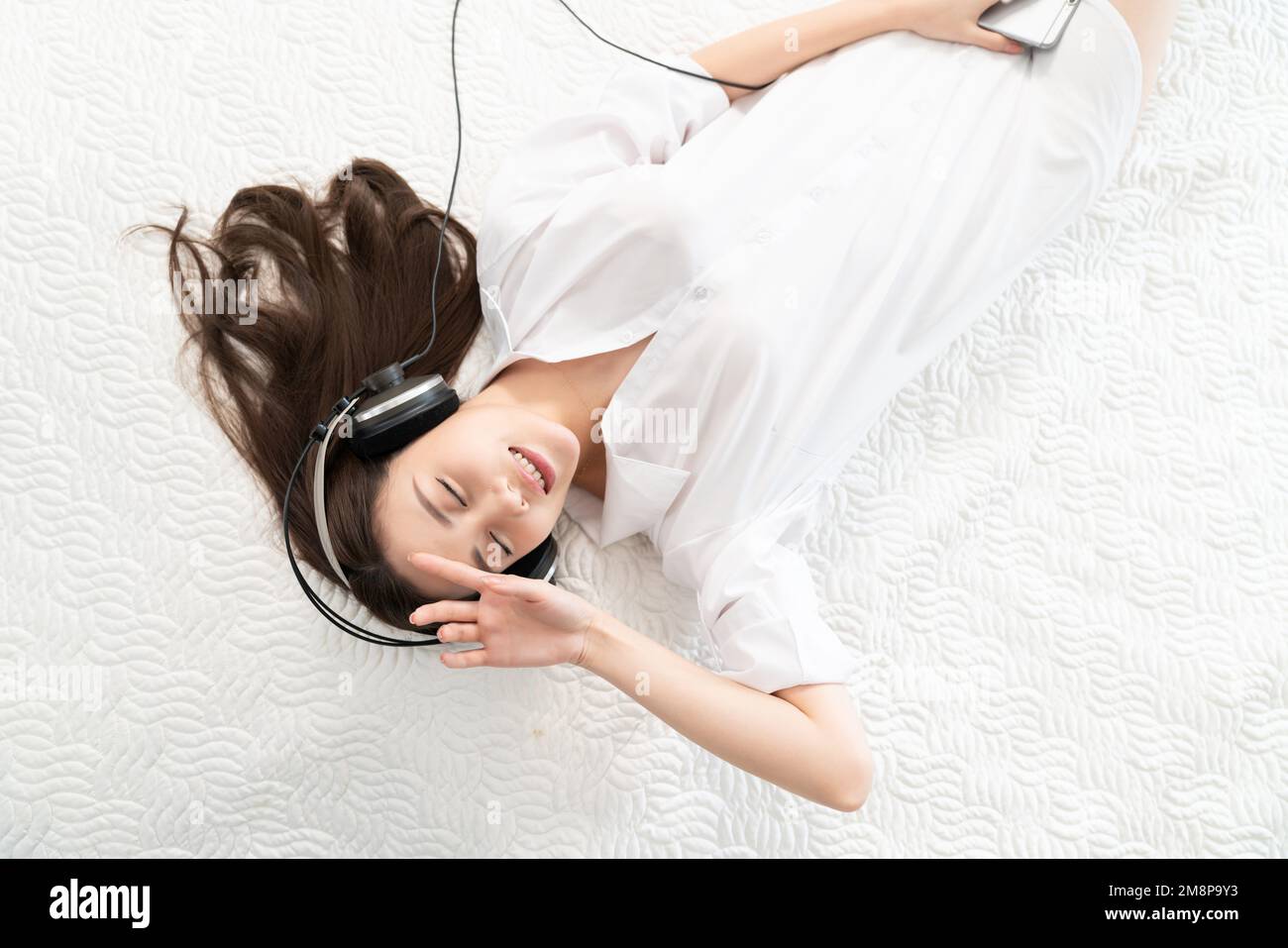 A young woman lying in bed listening to music Stock Photo - Alamy