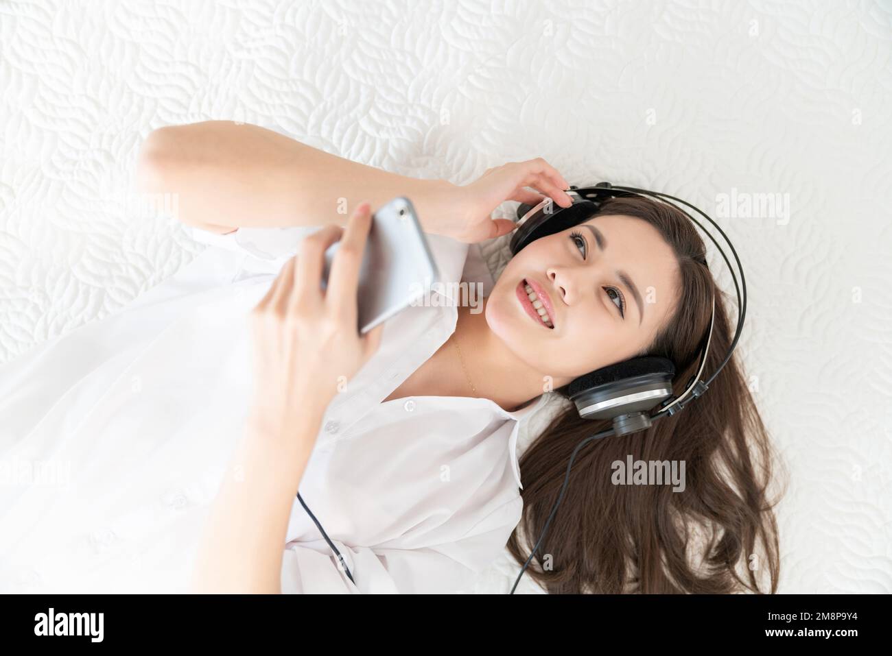 A young woman lying in bed listening to music Stock Photo - Alamy