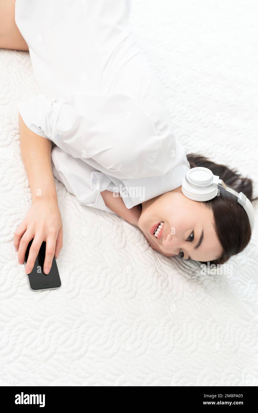 A young woman lying in bed listening to music Stock Photo - Alamy