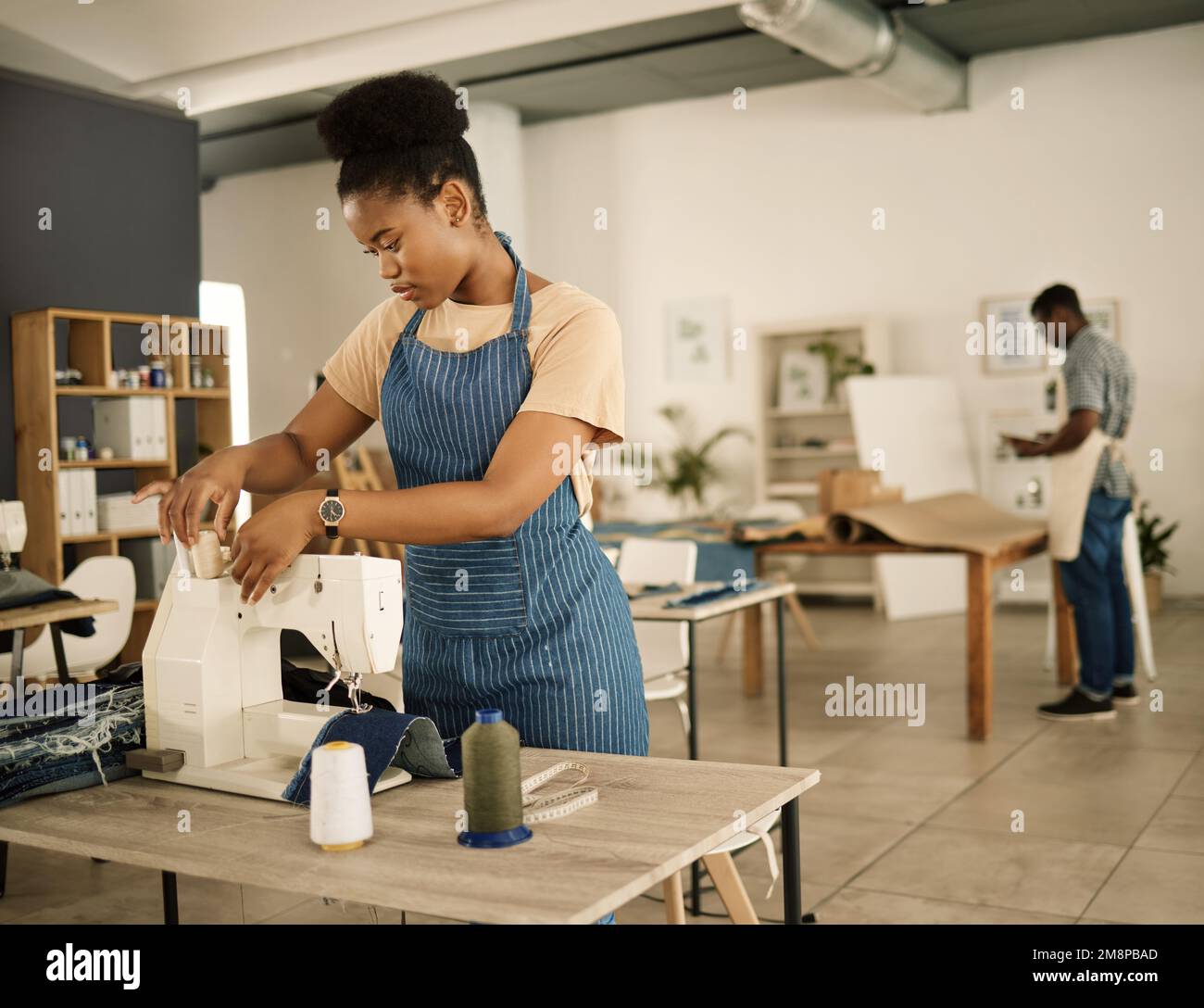 fashion designer threading needle on a sewing machine. Young tailor using sewing machine. Seamstress getting her sewing machine ready. African Stock Photo