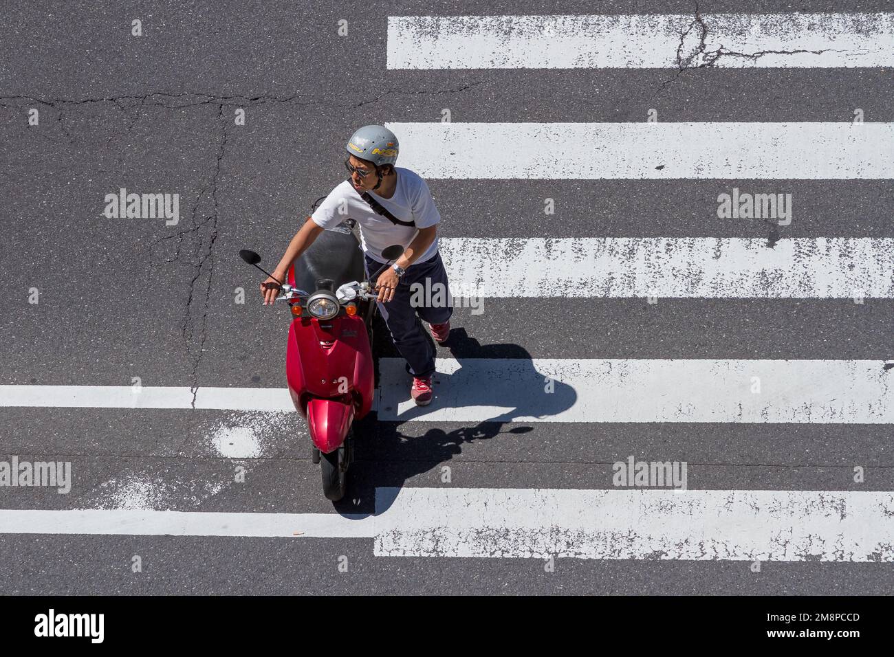 A young Japanese man pushes a moped across a pedestrian crossing in Ebisu, Tokyo, Japan. Stock Photo