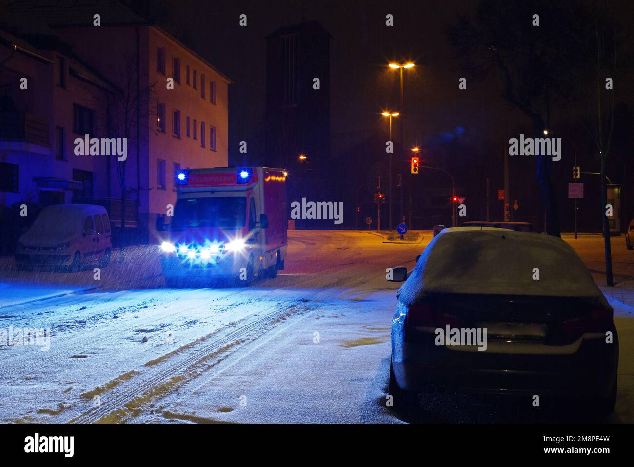 Ein Rettungswagen faehrt mit Blaulicht in der Nacht durch eine leere, verschneite Strasse in der Stadt. Stock Photo