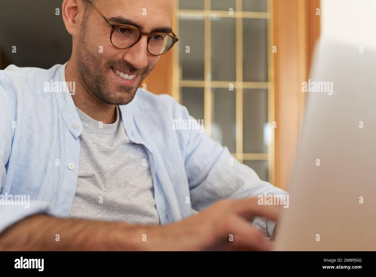 Young male with glasses smiling while using laptop Stock Photo