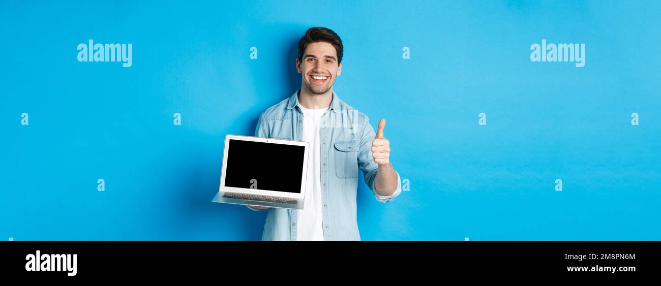 Smiling handsome man showing laptop screen and thumb-up, like promo ...