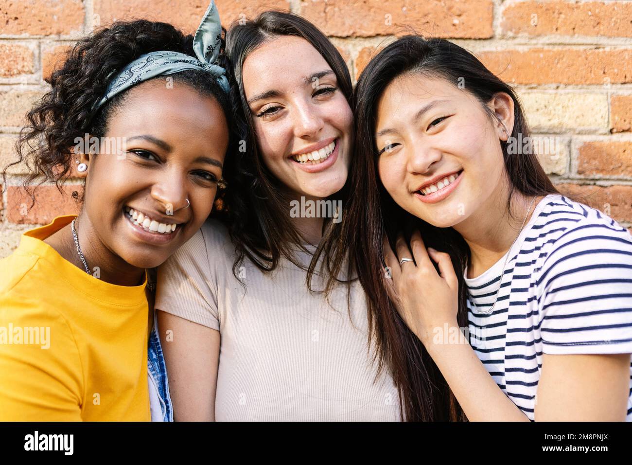 Smiling portrait of three young diverse female friends looking at camera outdoor Stock Photo