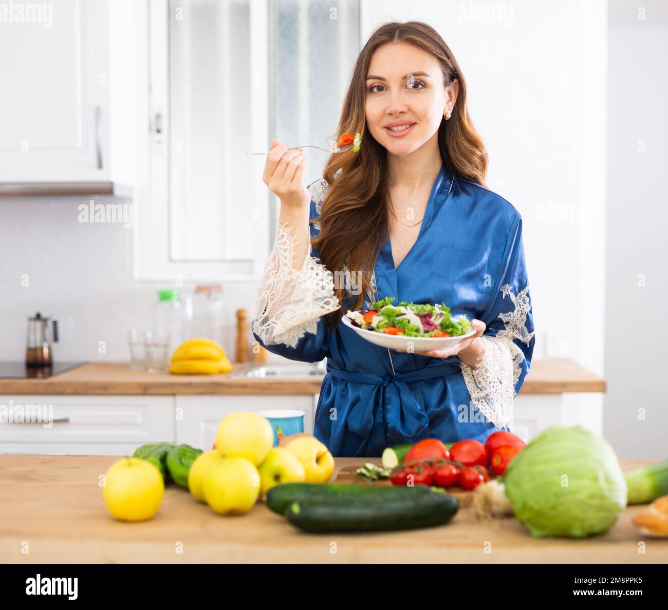 Positive housewife eating homemade salad in kitchen Stock Photo