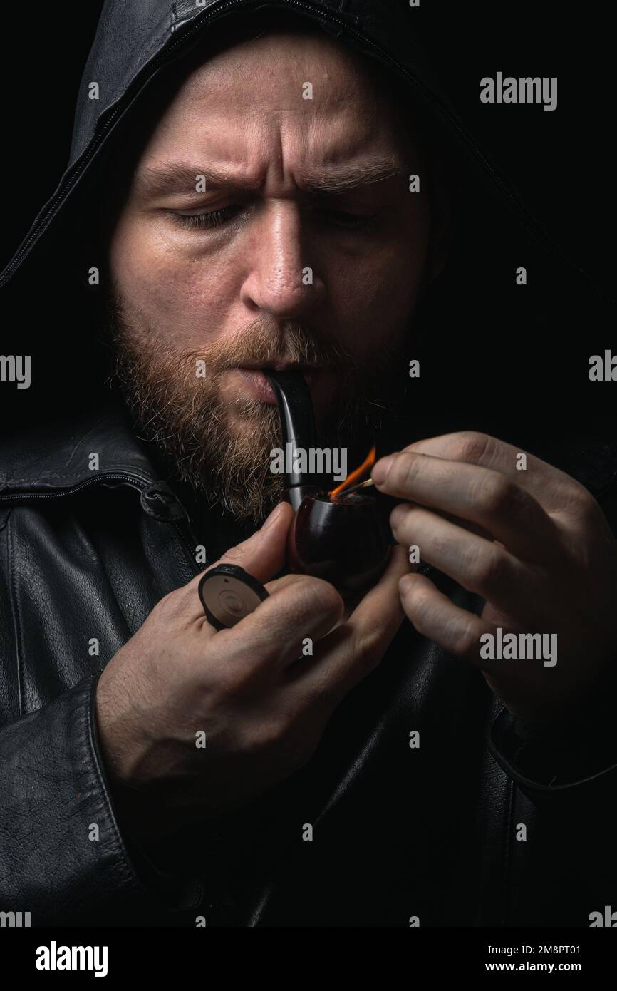 Portrait of a Bearded man in Black Rain Jacket Smoking a Pipe Stock