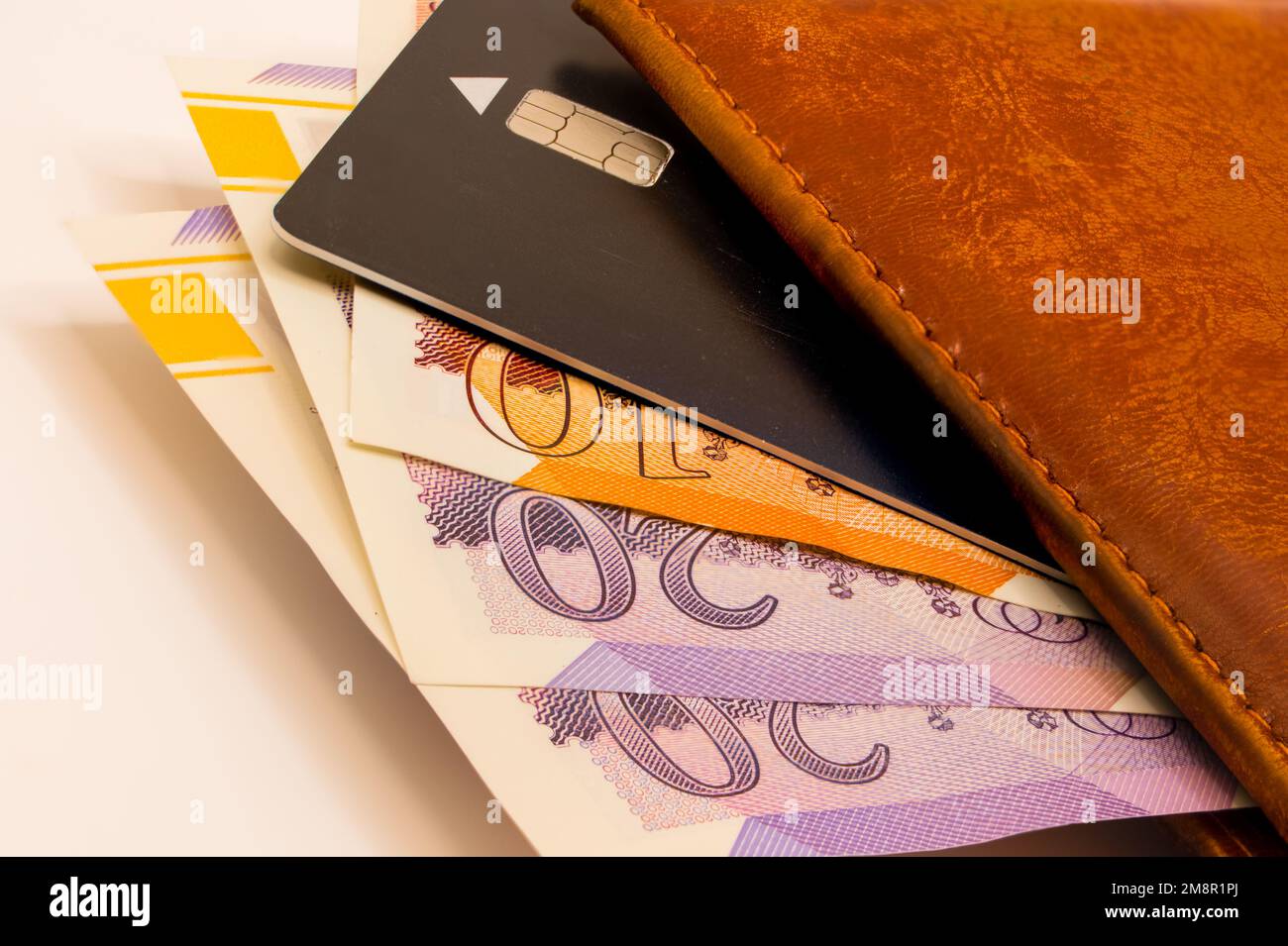 close-up of a pile of ten and twenty pound sterling notes with a brown leather wallet and black bank card Stock Photo