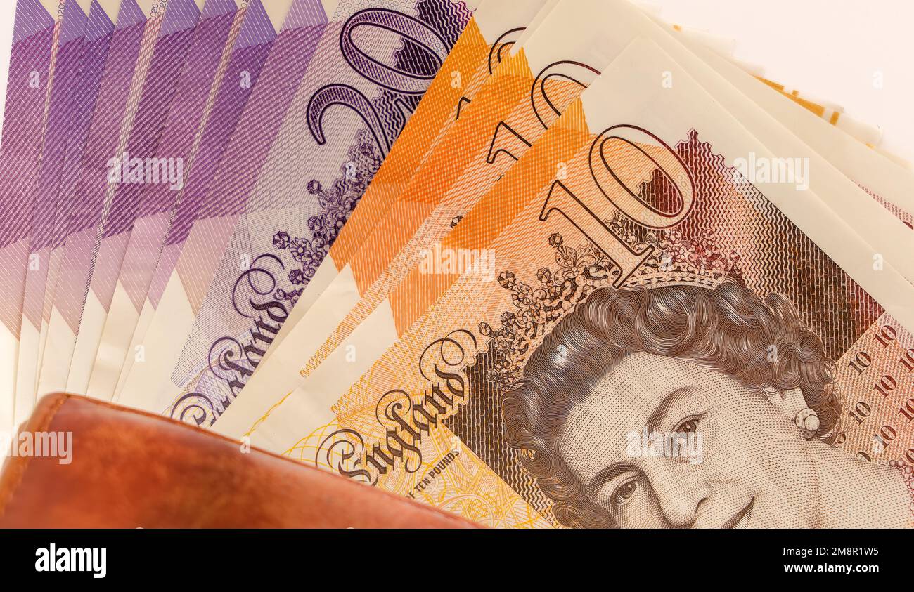 close-up of a pile of ten and twenty pound sterling notes with a brown leather wallet Stock Photo