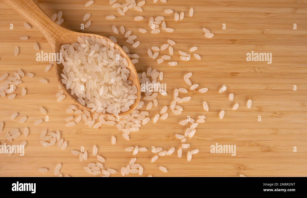 Grains Of Rice On A Wooden Floor, Top View. Raw Rice in Wooden Spoon For Menu Concept, Copy Space. Stock Photo