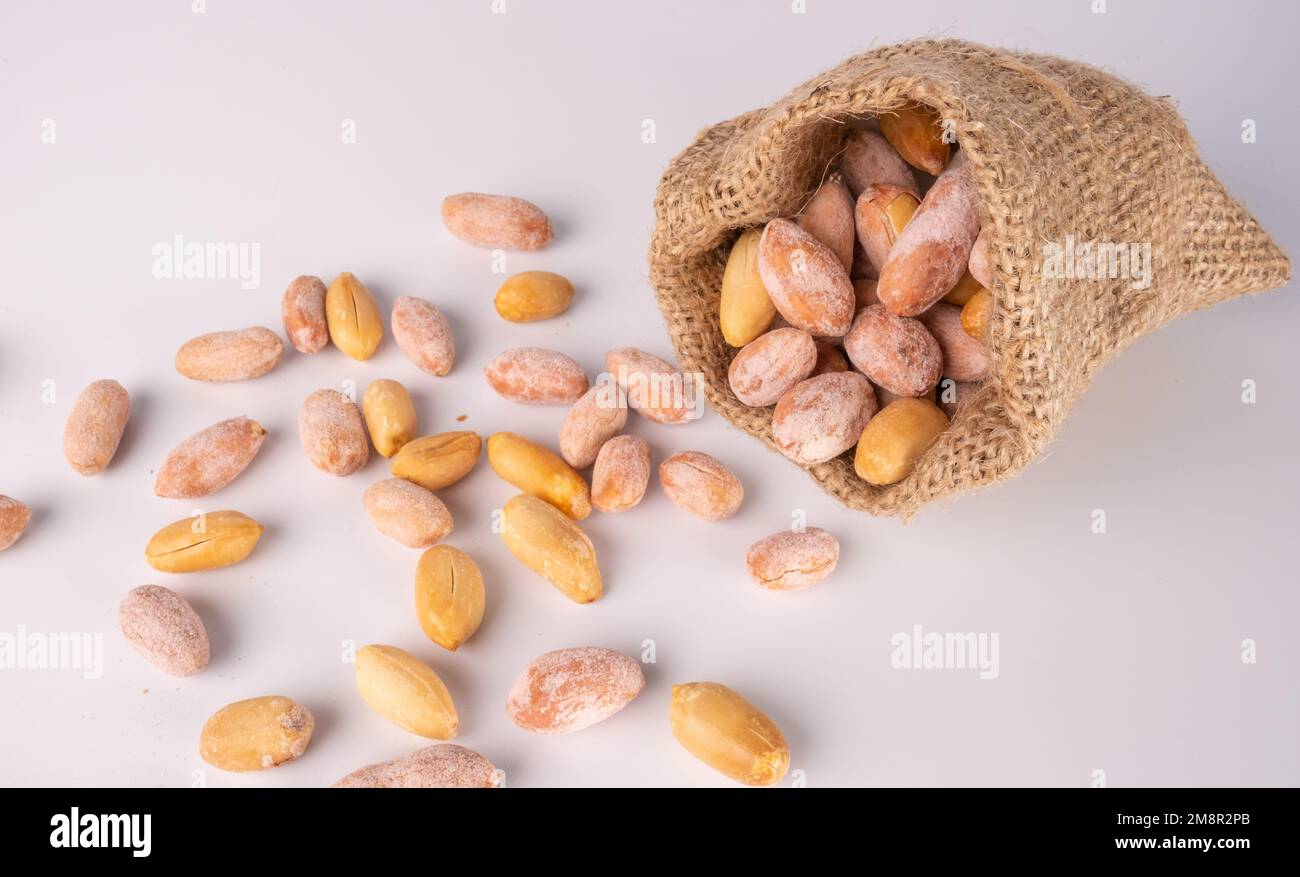 Peanuts in jute sack bag, white ground roasted peanuts poured. Stock Photo