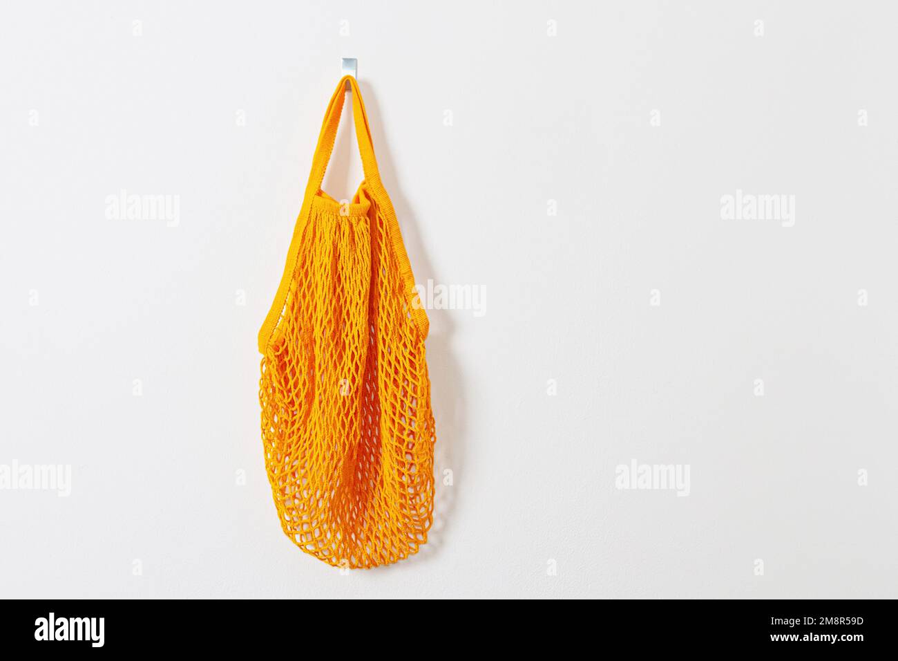 mesh grocery bag. Reusable bag. Vegetarianism, raw food diet, conscious consumption, grid. orange mesh bag hanging on a hook. Next to the keys. Go sho Stock Photo