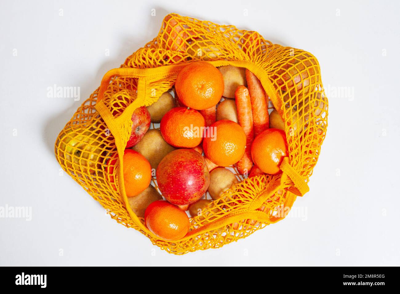 Orange mesh bag. View from above. Fresh vegetables and fruits from the farmers' market. Raw potatoes, raw carrots, apples, tangerines, oranges. Consci Stock Photo