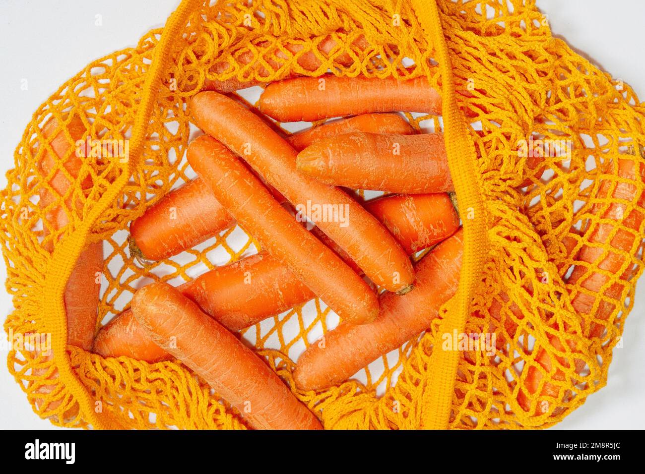 Mesh reusable bag with fresh carrots. Orange string bag. Raw carrots. View from above. Close-up. Vegetarian, raw food, fresh vegetables. Conscious con Stock Photo