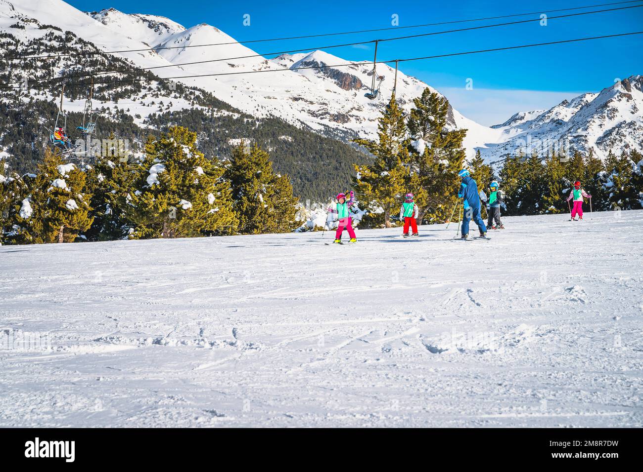 Ski instructor teaching a group of young kids how to ski in El Tarter green slope. Winter holidays in Andorra, Pyrenees Mountains, Grandvalira Stock Photo