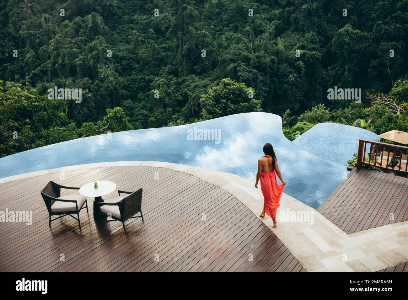 Aerial shot of young female model in sundress walking by the swimming pool. Woman at luxury resort poolside. Stock Photo