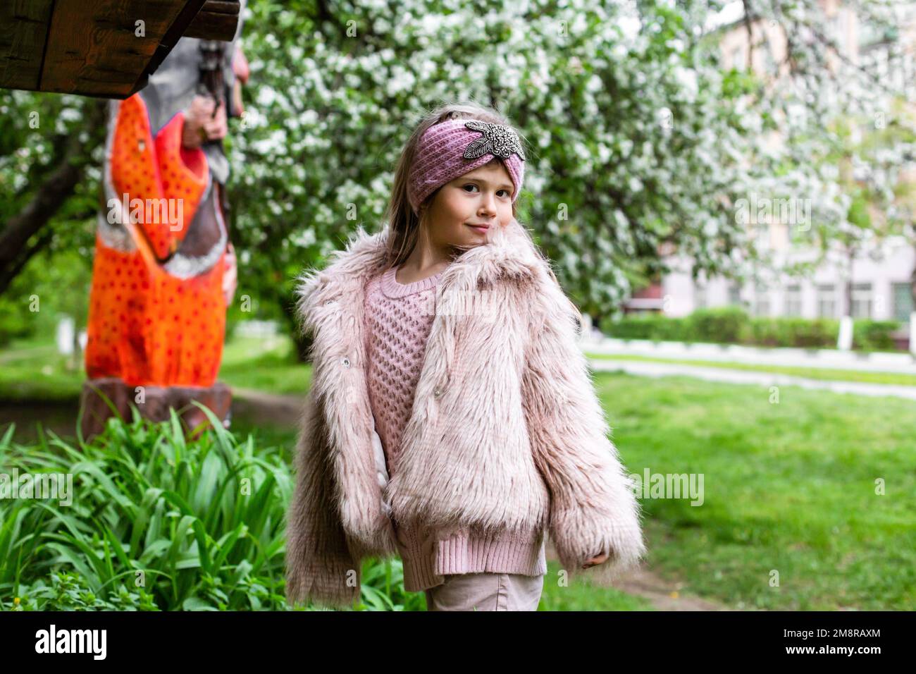 girl in a fluffy jacket walks in a park with blooming trees in spring