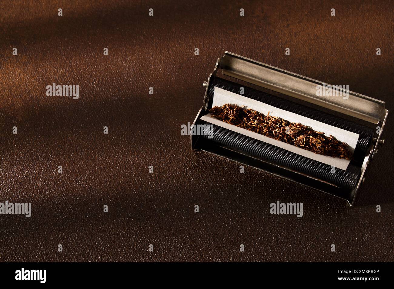 Handrolled cigarette, rolling machine, scattered tobacco on background