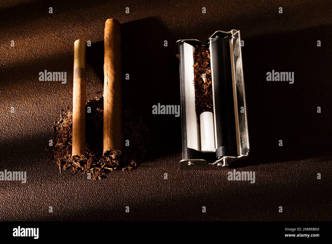 Rolling machine, cigarillos, scattered tobacco on background, cigarette