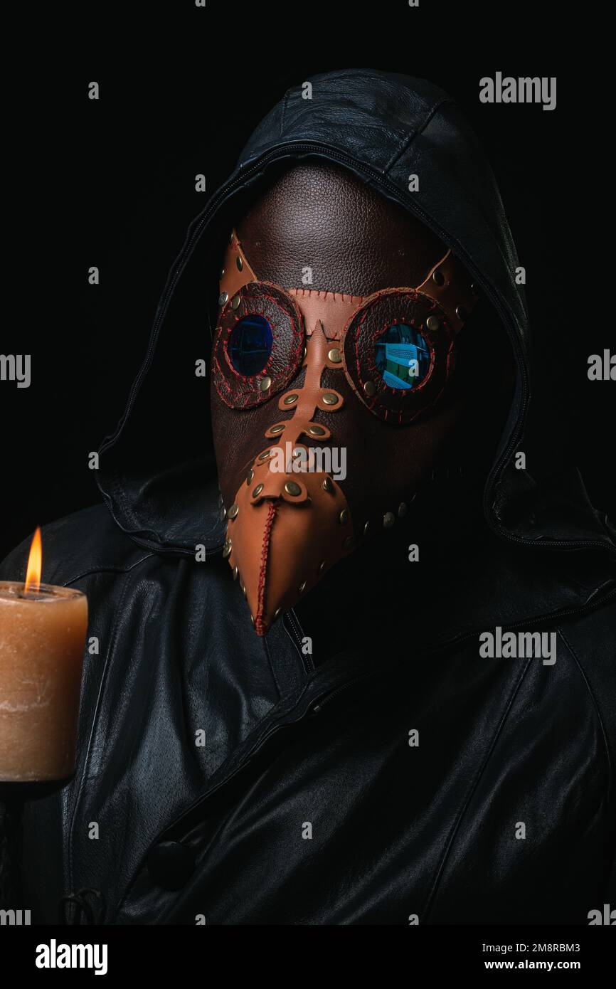 Plague doctor with crow-like mask and candle isolated on black ...