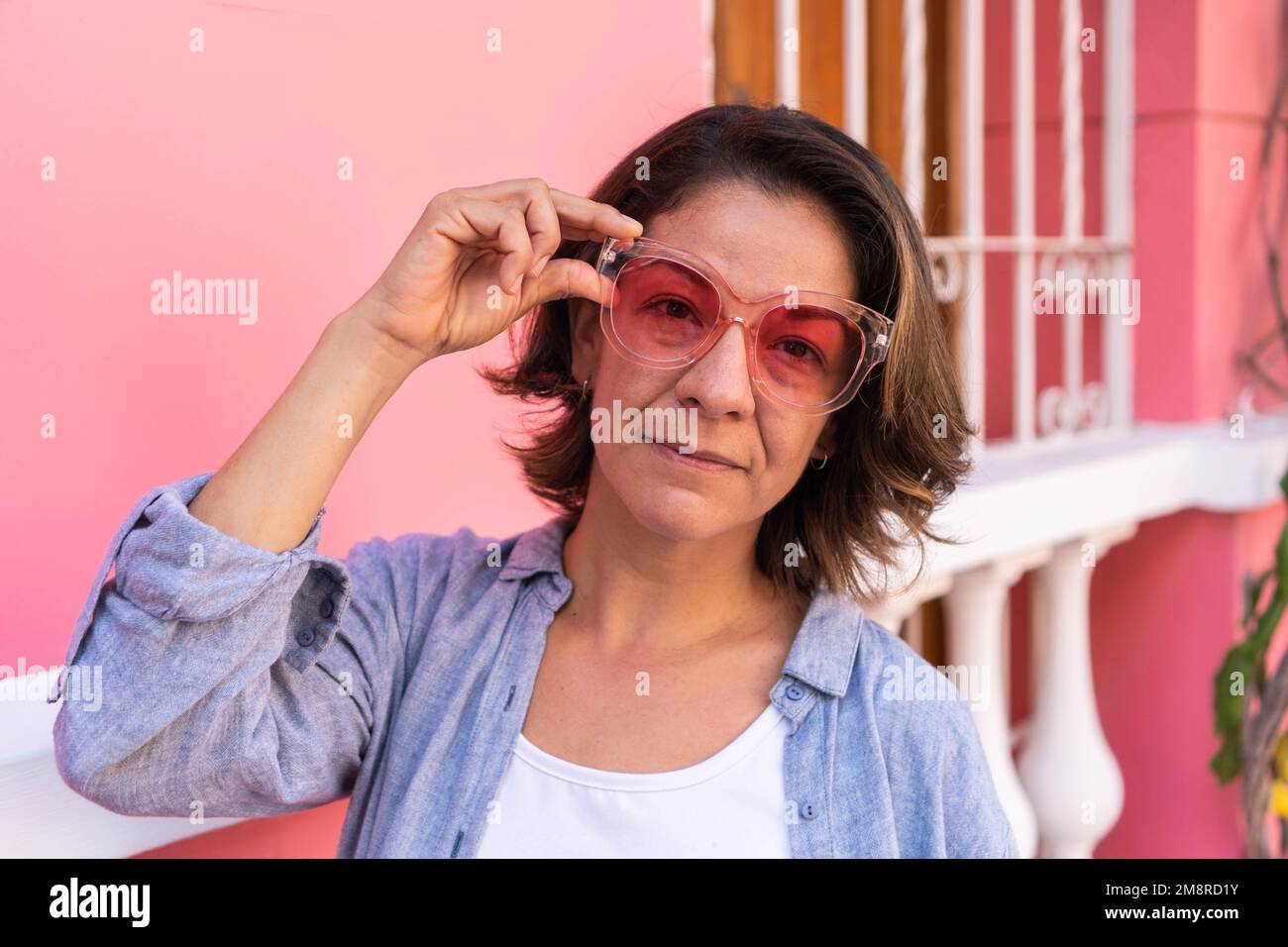 Self assured young lady adjusting sunglasses and looking at camera