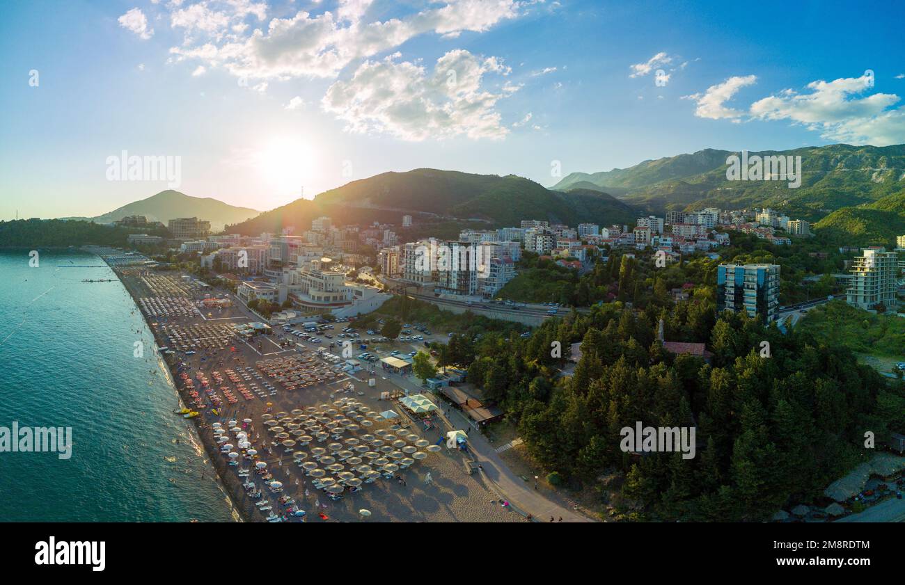 Panorama of sandy beach with sun umbrellas, plastic sunbeds and people relaxing in swimsuits in the historic tourist resort town of Becici near Adriat Stock Photo