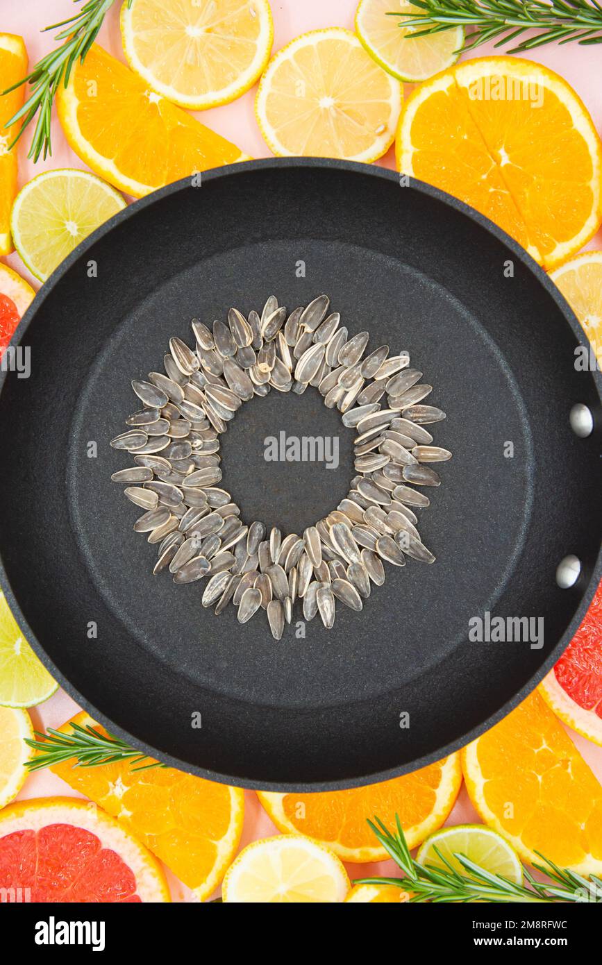 background of slices of citrus fruits, oranges, lemons, limes, grapefruits, on which a black pan is placed, inside which a sunflower flower is made fr Stock Photo