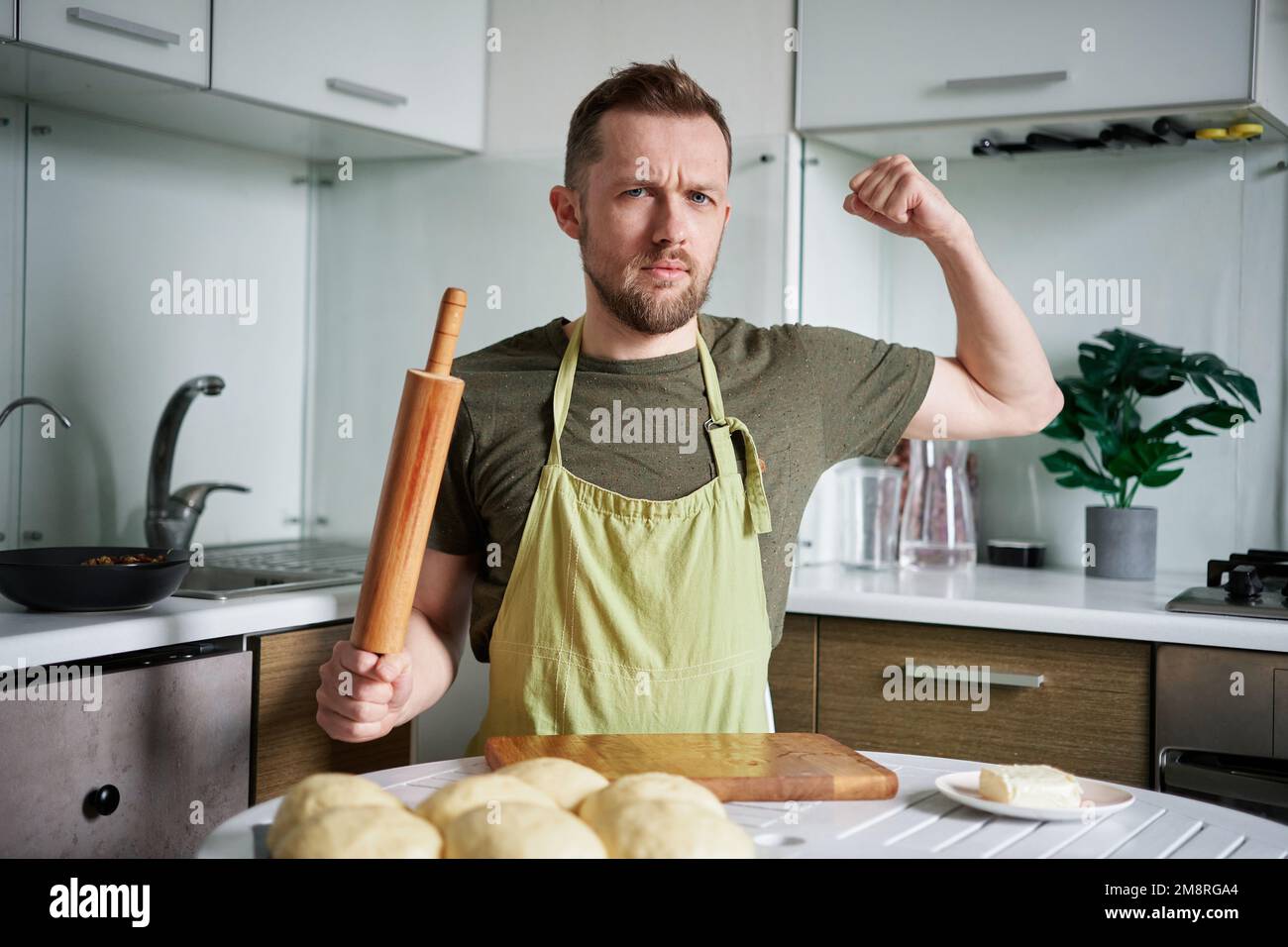 Handsome male baker at home sitting at the table with rolling pin