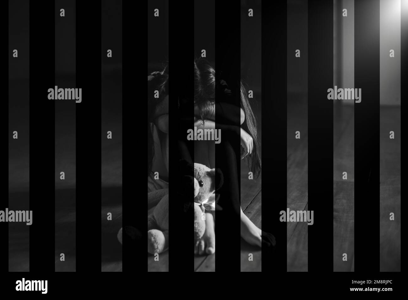 A little girl locked up in a dark prison room sitting sad and desperate