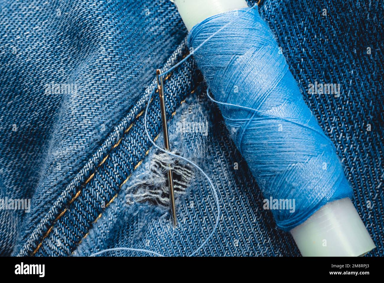 A needle and thread sew up a hole in a denim. Work of a seamstress