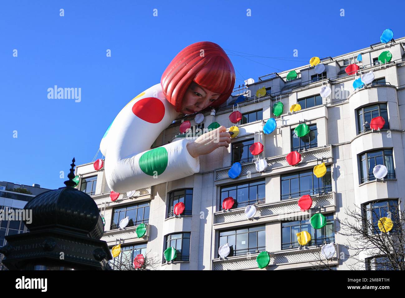 Paris, France. 15th Jan, 2023. People stop on a sunny day to take photos and view the giant sculpture of artist Yayoi Kusama as it hangs over the top of the building as part of a collaboration between Louis Vuitton and the world-renowned Japanese artist Yayoi Kusama in Paris, France on Jan. 15, 2023. (Photo by Lionel Urman/Sipa USA) Credit: Sipa USA/Alamy Live News Stock Photo