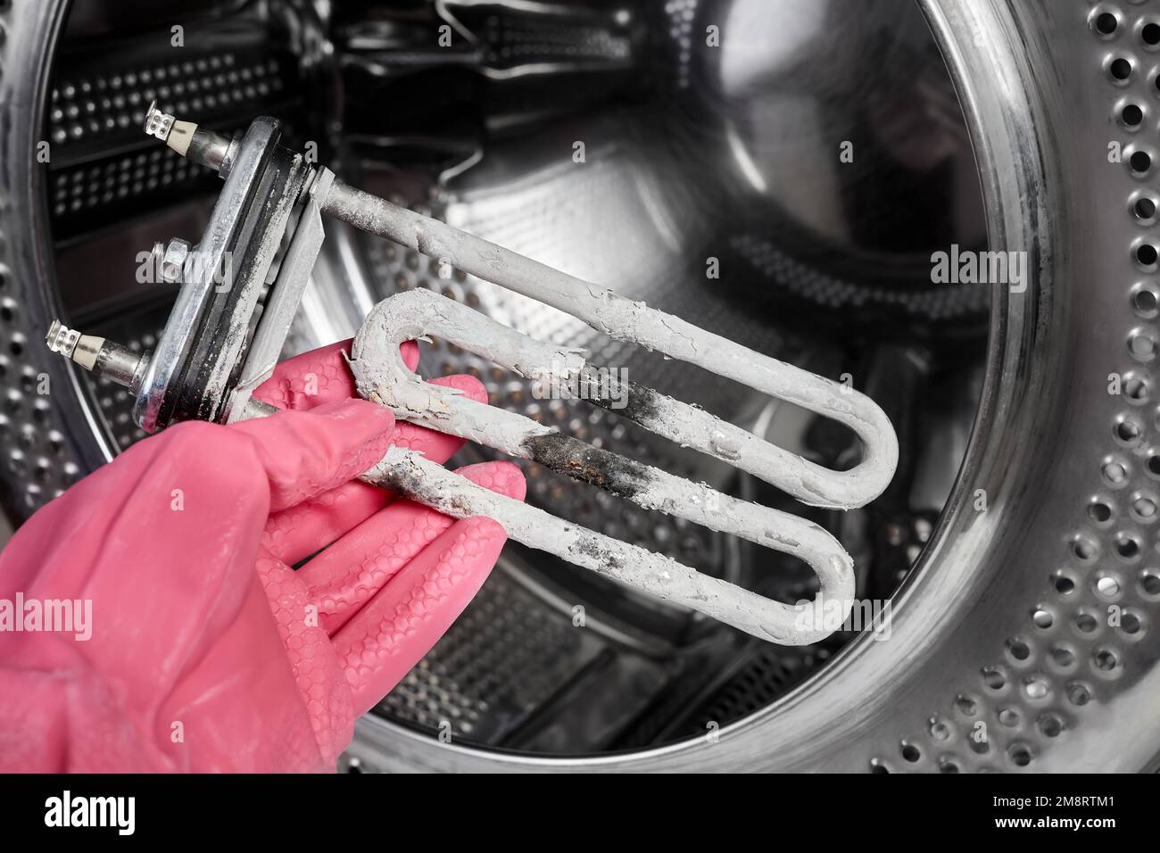 A man holds in his hand a burntout heating element of a washing