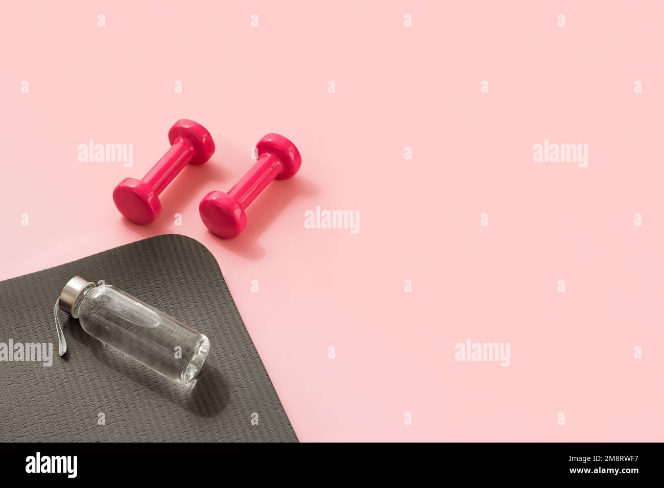 Stylish gray and pink fitness training and gym concept. Perspective view of gray sport mat, water bottle and pink dumbbells on pink background. Set for pilates, fitness with copy space Stock Photo
