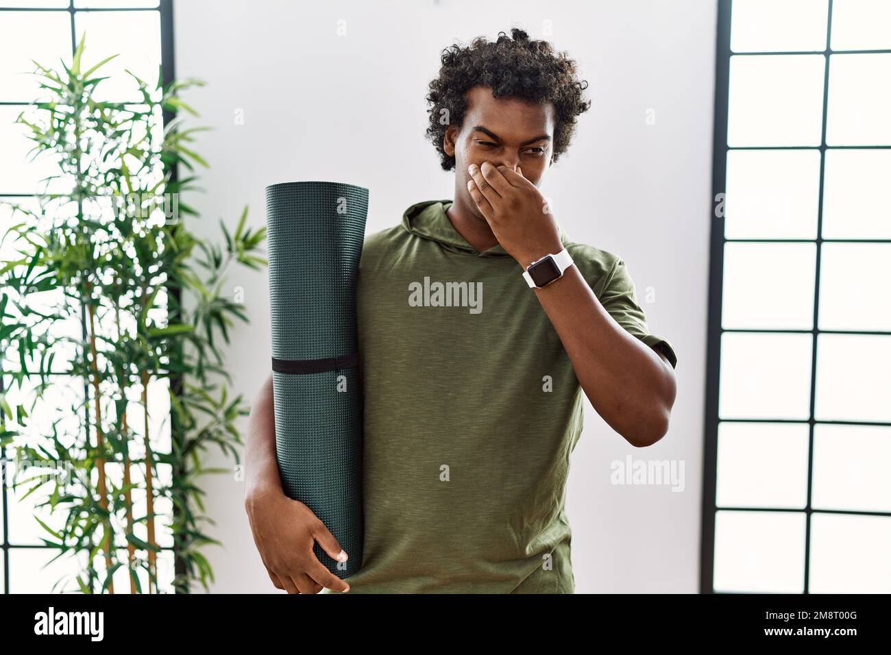 African man with curly hair holding yoga mat at studio smelling