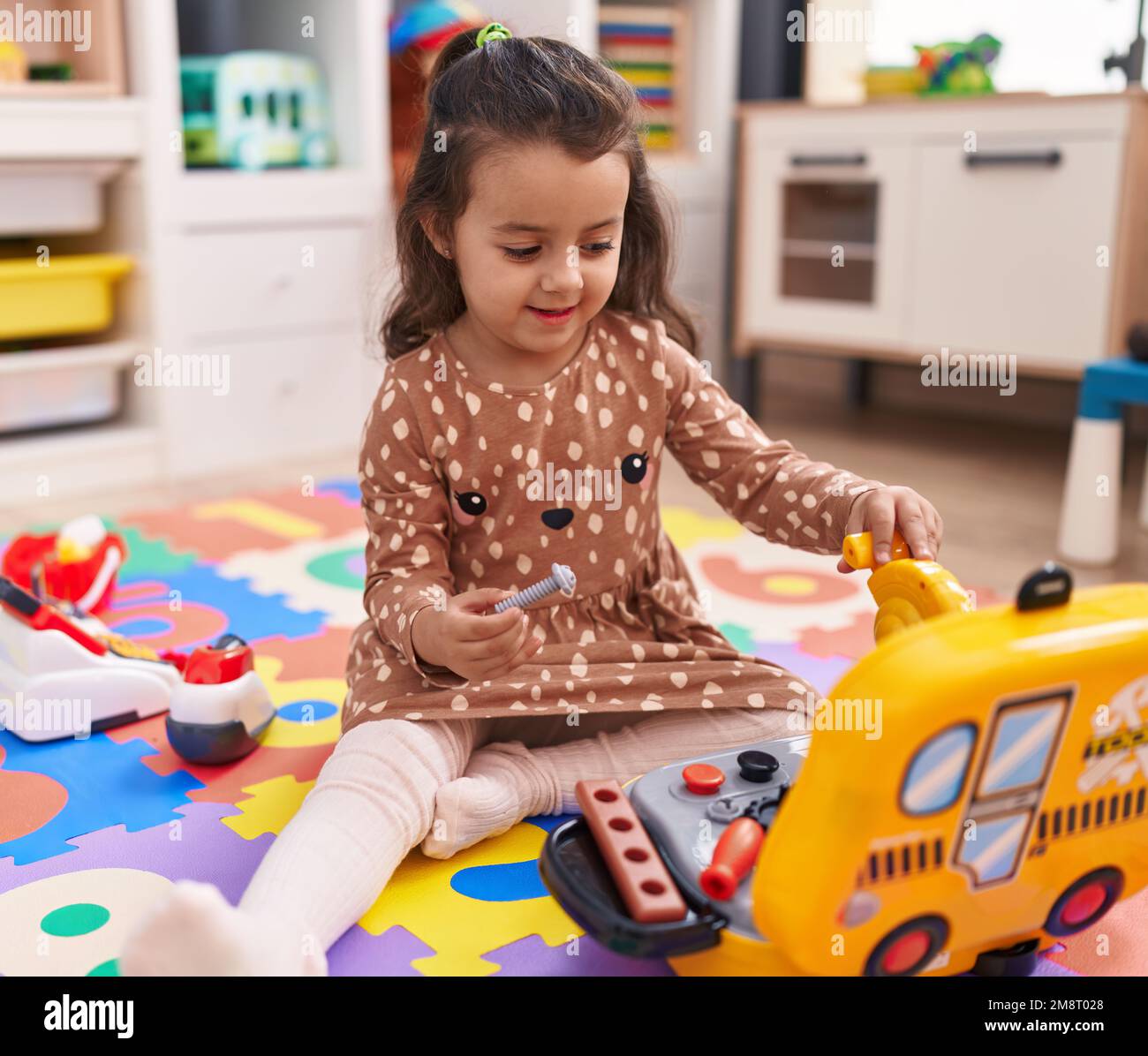 Adorable hispanic girl sitting on floor playing with mechanic toy at ...