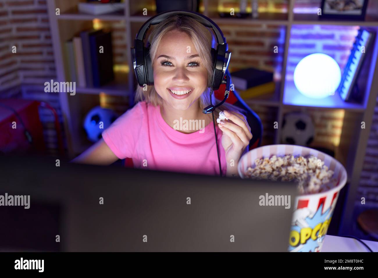 Young blonde woman streamer playing video game eating popcorn at