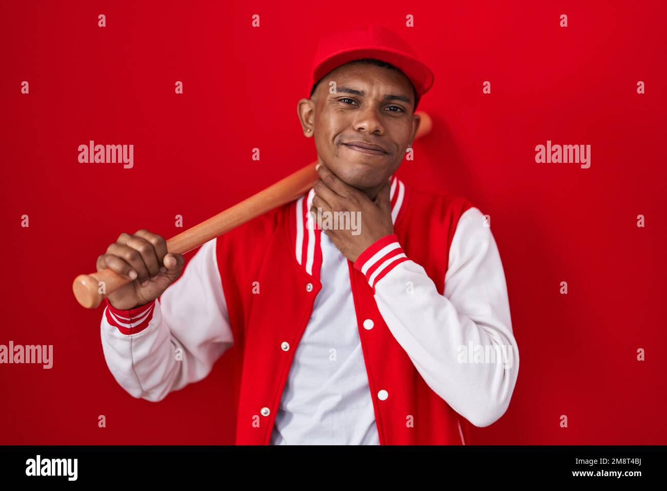 Young hispanic man playing baseball holding bat touching painful neck ...