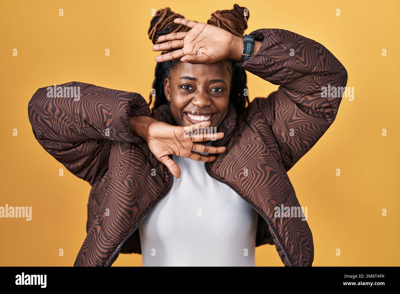 African woman with braided hair standing over yellow background smiling ...