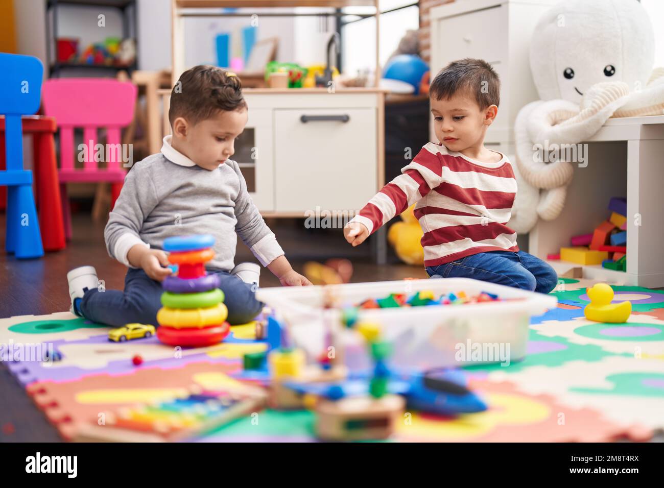 Two kids playing with toys sitting on floor at kindergarten Stock Photo ...