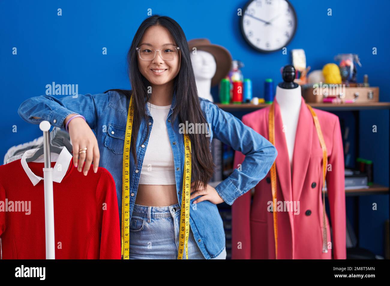 Young chinese woman tailor smiling confident leaning on clothes rack at ...