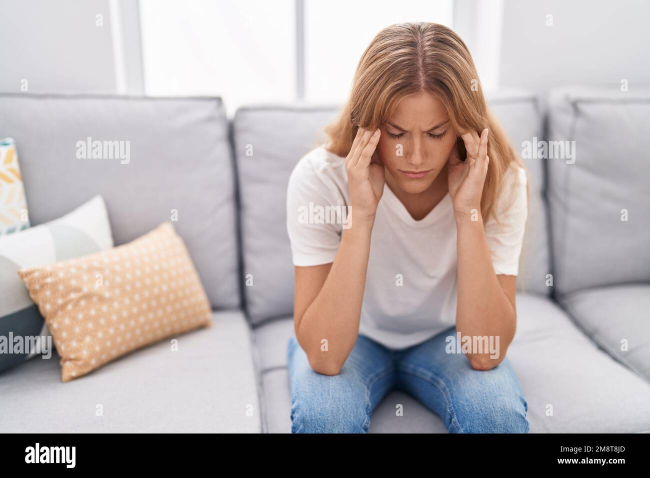 Young blonde girl stressed sitting on sofa at home Stock Photo - Alamy