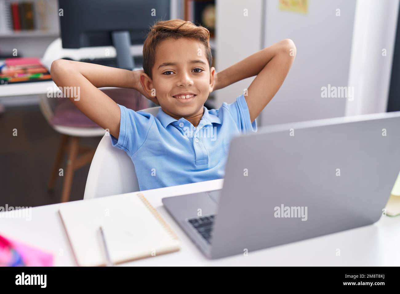 Adorable hispanic boy student using computer relaxed with hands on head ...