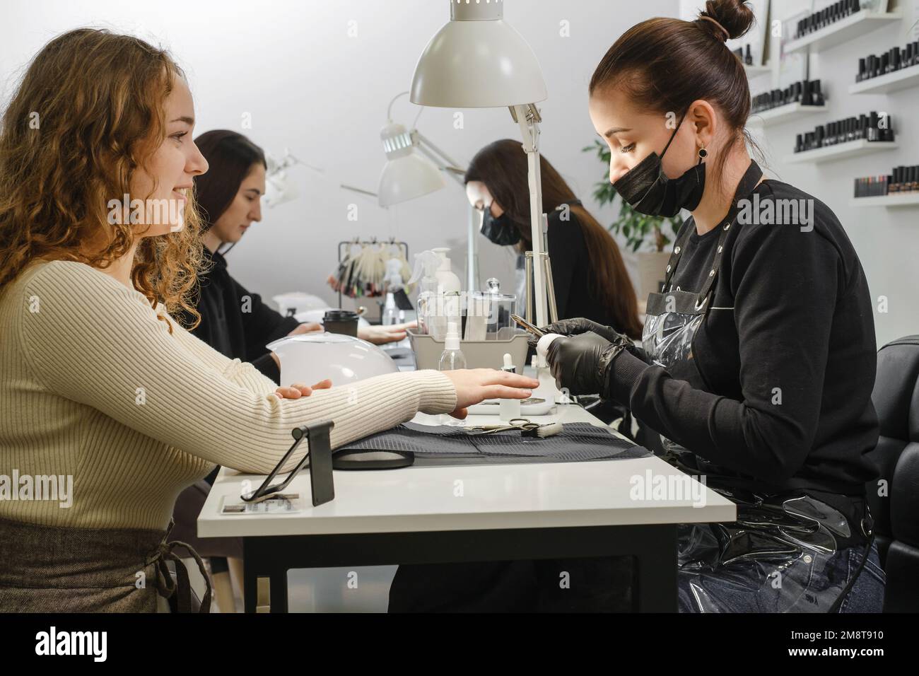 Doing manicure in salon. Female manicurist working on client nails in professional salon. Occupation concept. Customers at beauty green modern studio  Stock Photo