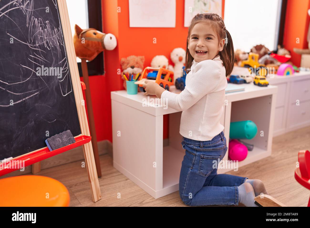 Adorable hispanic girl playing with truck toy sitting on floor at ...
