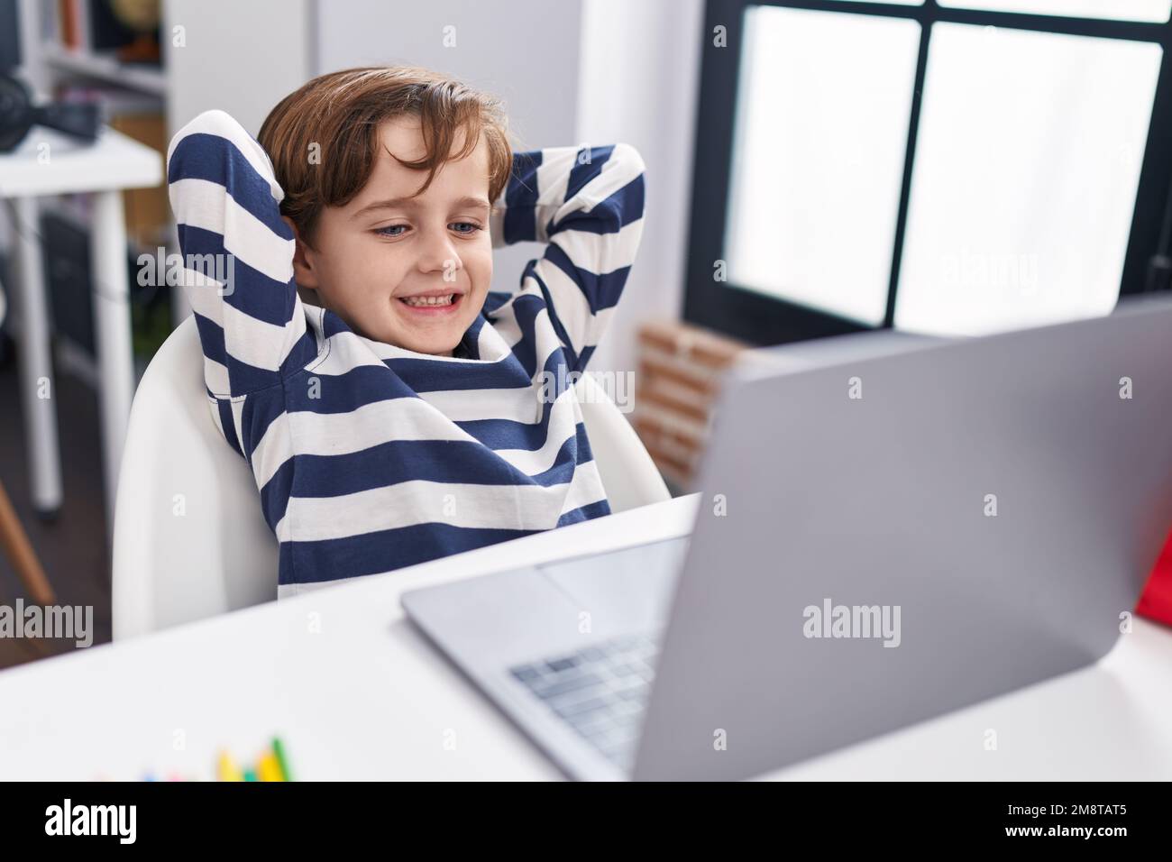 Adorable hispanic boy student using computer relaxed with hands on head ...